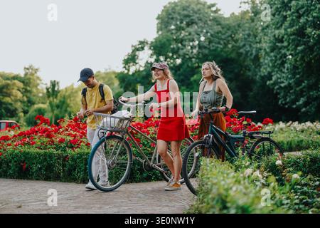 Three friends walking bicycles through a flower-filled park in the Netherlands on a summer day Stock Photo