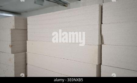 Close-up, angled view of stacked white autoclaved aerated concrete blocks. The minimalist composition highlights the porous, rough texture of the buil Stock Photo