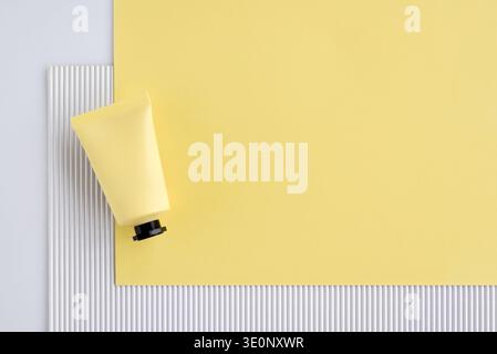 Bright yellow minimalist flat lay with cosmetic tube on ribbed white texture and large yellow paper background. Ample copy space for text. Stock Photo