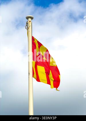 northumberland flag featuring thick vertical red and yellow stripes waves from a light-colored flagpole against a bright, cloudy expanse Stock Photo
