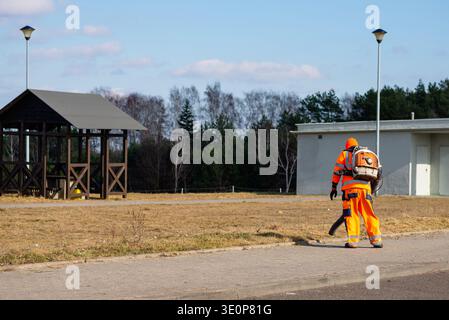 Professional gardener in orange protective suit clearing a wooden rest area in a park using specialized power equipment. Stock Photo