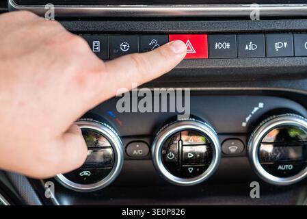 Close up of a driver activating emergency hazard warning signal in a vehicle for road safety and caution. Stock Photo