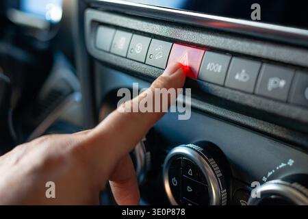 Close up of the red triangle hazard button being pressed on a vehicle console during an emergency or stop. Stock Photo