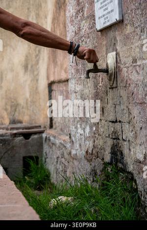 Hand turning old water faucet on weathered stone wall Stock Photo