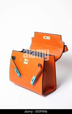 Stylish miniature orange leather handbag with open top, black interior lining, gold-tone hardware and bright turquoise details on handles. Stock Photo
