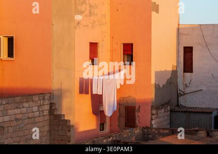 White sheets hanging to dry between orange and peach colored houses. Warm sunset light creates geometric shadows on the facades. An atmosphere of dome Stock Photo