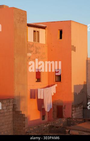 White sheets hanging to dry between orange and peach colored houses. Warm sunset light creates geometric shadows on the facades. An atmosphere of dome Stock Photo