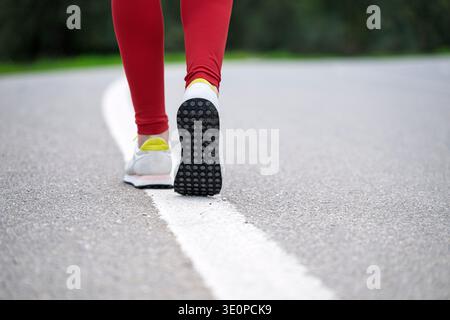 Close up of a woman runner walking along a road wearing white sneakers and red leggings Stock Photo