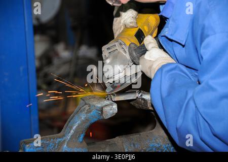 Close-up of a worker using an angle grinder to cut or polish metal in a vise, producing bright sparks during a mechanical workshop task. Stock Photo