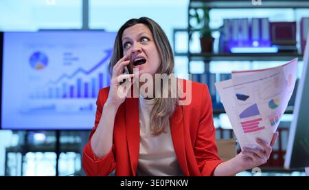 Businesswoman multitasking in a vibrant office environment while on a call discussing important financial trends Stock Photo