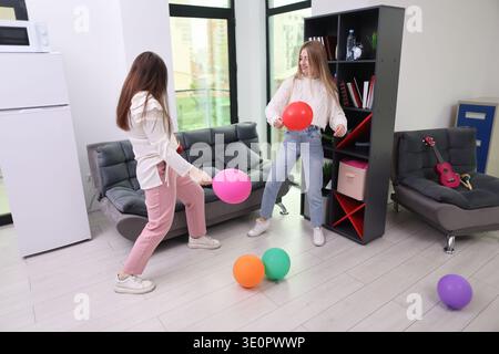 Two friends enjoy a lively moment playing with colorful balloons indoors in a bright and cheerful setting Stock Photo