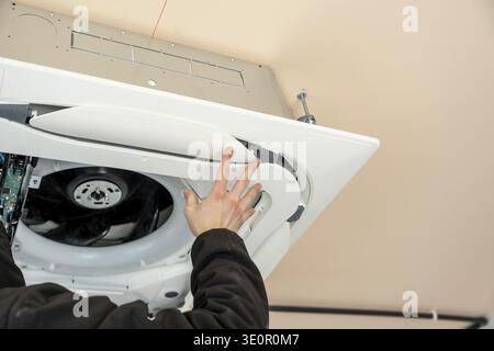 Air conditioning technician installing a new indoor ceiling cassette unit for hvac system, working on the ventilation grilles and electrical component Stock Photo
