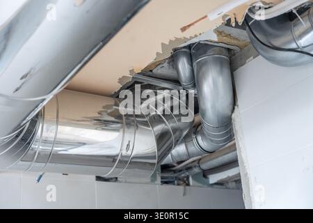 Exposed metal ventilation ducts and pipes connecting a new air conditioning system in a commercial or residential building, showing ongoing constructi Stock Photo