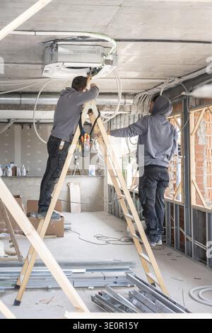 Air conditioning technicians installing a new hvac system at the ceiling during the construction phase of a building, performing electrical connection Stock Photo