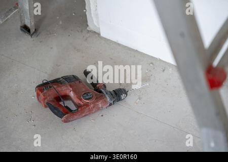 Rotary hammer drill lying on a dusty concrete floor in a room under renovation, indicating ongoing construction, demolition, drilling, and building ac Stock Photo