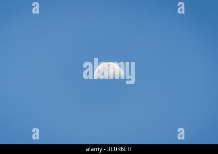 Minimalist nature scene showing the half Moon in a clear blue daytime sky. Peaceful celestial background. Stock Photo