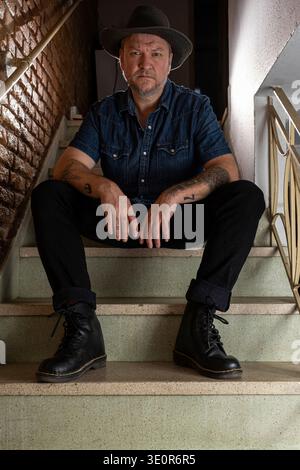 A 48 year old Brazilian man sits on a ladder and staring directly at the camera. Stock Photo
