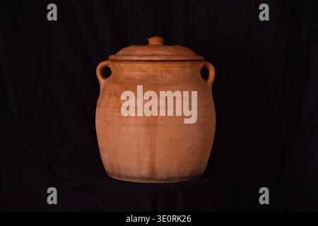 Terracotta earthenware clay cooking pot with handles and lid on black background Stock Photo