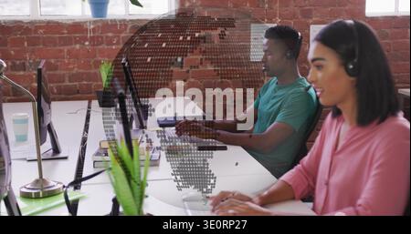 Typing woman in pink blouse and headset at shared desk, monitors, dotted globe overlay, copy space Stock Photo