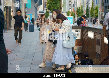 Tokyo, Japan - Oct 14 2024, panoramic view of two women staring at their phones going out from an underground passageway, with many people in the back Stock Photo