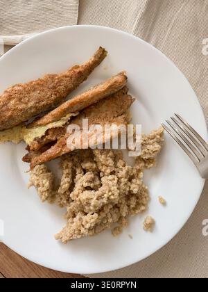 A healthy breakfast is displayed on a white plate. Baked bran with porridge is served alongside fried fish. The setting is on a wooden table with a si Stock Photo