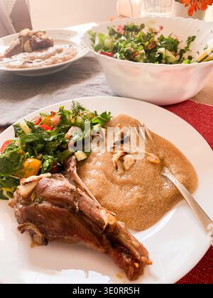 A person eats a breakfast of rabbit meat served with amaranth porridge and a fresh salad made of colorful vegetables. The meal is placed on a bright t Stock Photo