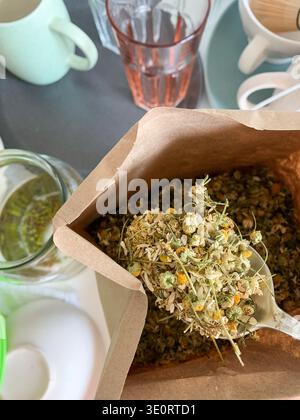 A paper bag holds chamomile herbs ready for brewing. The background shows glassware and cups organized on a kitchen table. The setting looks inviting Stock Photo