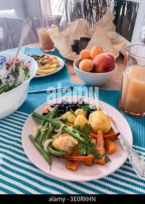 A table displays a healthy breakfast with baked potatoes, sweet potatoes, carrots, green beans, salad, and fresh fruit like apricots and peaches, perf Stock Photo
