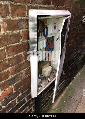 electric junction box with door prized open mounted on a brick wall down a back alley in town Stock Photo