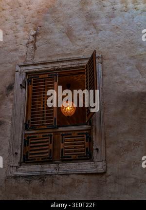 Croatia, Europe: stone wall and crystal chandelier with the light on glimpsed from a wooden shuttered window in the alleys of the old town of Split Stock Photo