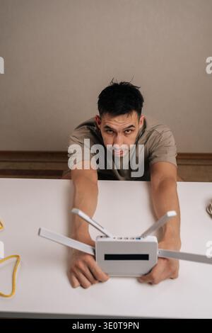 Vertical portrait of technician holding white wireless internet router with multiple antennas, looking at camera while setting up the device for Stock Photo