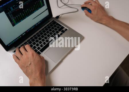 Close-up of person working on laptop computer with wired mouse, typing on keyboard and navigating digital audio workstation interface, concept of Stock Photo