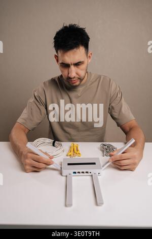 Vertical portrait of technician male examining a wireless router and ethernet cables on a white table, focusing on internet setup and network Stock Photo