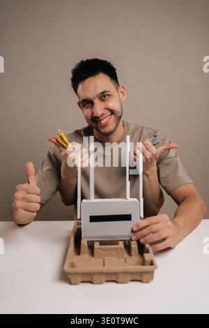 Vertical portrait of enthusiastic man setting up new wireless internet router, holding essential ethernet cables and network adapter for home Stock Photo