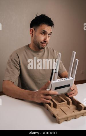 Vertical shot of technician holding new white wireless router, studying setup and placement for optimal home wifi performance and stable internet Stock Photo