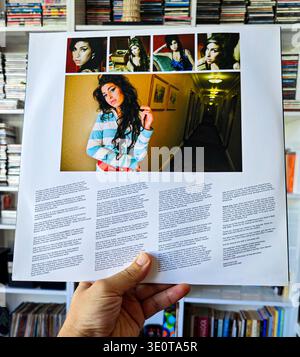Hand holding the back cover of Amy Winehouse's Back to Black vinyl record featuring a photo collage and album credits. Stock Photo
