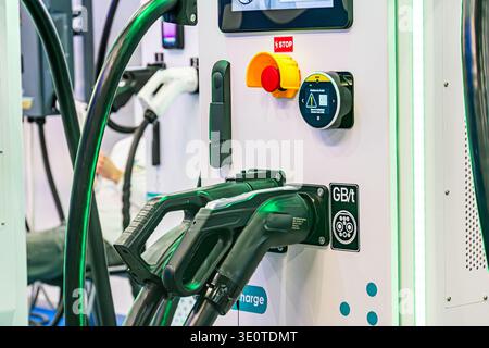 Close-up view of an electric vehicle charging station Dark green electrical socket connected to a cable, adjacent small control panel with buttons red Stock Photo