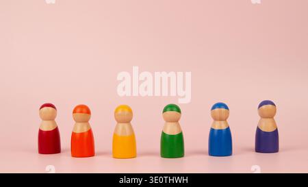 Colorful wooden figurines arranged in row on pink background. Each figure has distinct rainbow color: red, orange, yellow, green, blue, and purple Stock Photo