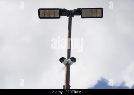 Upward perspective of a metal light pole with two LED lamps and surveillance cameras installed together above an outdoor commercial property Stock Photo