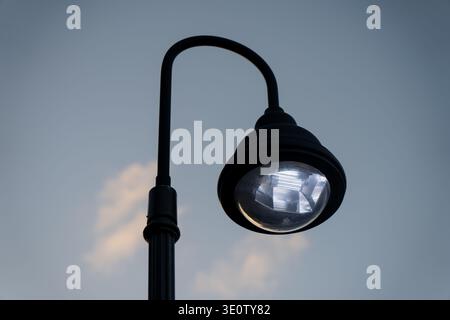 Minimal upward perspective of a black ornamental street light featuring a curved support arm and reflective glass housing Stock Photo