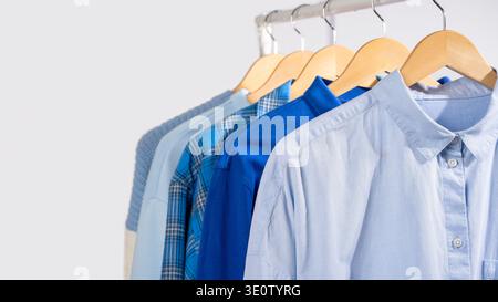 Close up blue shirts hanging on wooden beige hangers on clothing rack, light gray background. Concept of capsule wardrobe, minimalist clothing basics Stock Photo