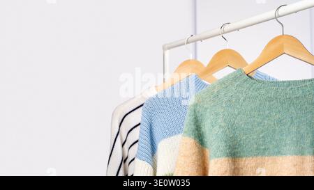 Colorful knitted woolen sweaters hanging on wooden hangers clothing rack, light gray background. Concept of winter clothing sale, seasonal fashion dis Stock Photo