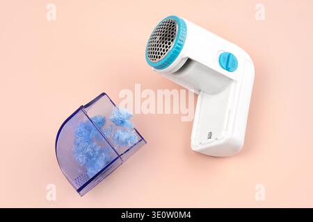 Modern fabric shaver with removable lint container and collected blue fuzz on pastel pink background. Concept of smart electric device, tool for remov Stock Photo