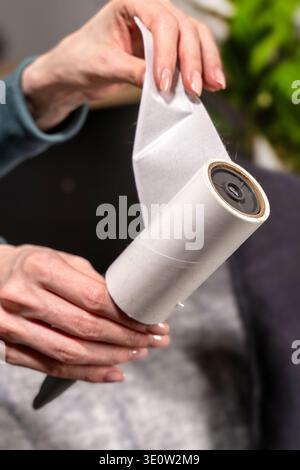 Close up hands peeling used sheet from adhesive lint roller after sofa and pillow cleaning. Concept of textile hygiene and household cleaning routine Stock Photo