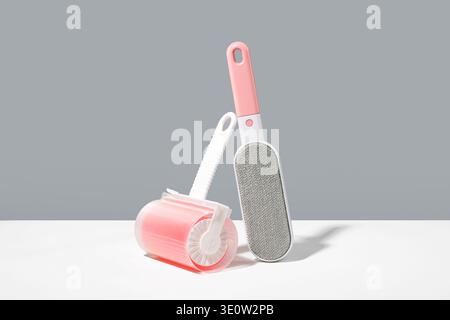 Two cleaning tools, eco pink lint clothing roller and fabric brush with gray surface on white table, minimalistic light gray background. Creative conc Stock Photo