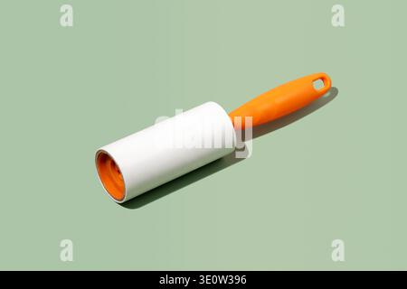 Adhesive lint roller with orange handle on green background in studio hard lighting. Concept of household cleaning tool for sticky tape removal, garme Stock Photo
