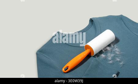 Lint roller with an orange handle rests on a blue long-sleeve shirt, displaying collected lint and hair fibers on a light gray background, emphasizing Stock Photo