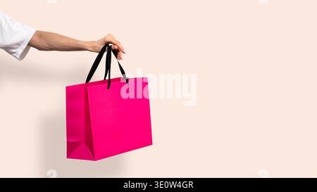 Woman holding in hand bright pink paper shopping bag on light pastel beige background. Concept of shopping discounts offer promotion, delivery sale pu Stock Photo