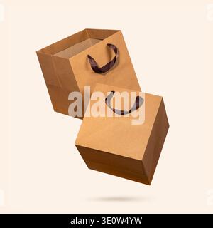 Two square kraft paper shopping bags with brown fabric handles flying on light beige background. Concept of eco-friendly packaging, sustainable shoppi Stock Photo