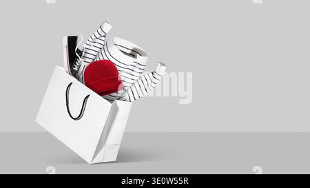 White shopping bag filled with clothing and shoes on soft gray background. Concept of seasonal fashion sale, online shopping, clothing delivery and wi Stock Photo